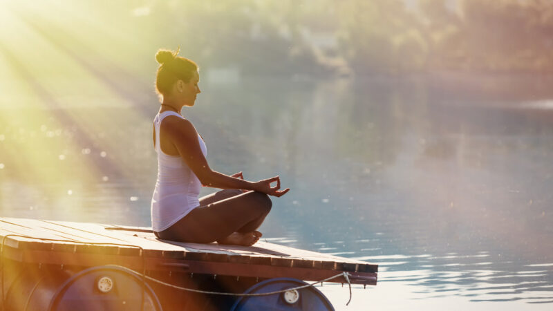 湖畔でヨガをする女性。呼吸法を実践中。