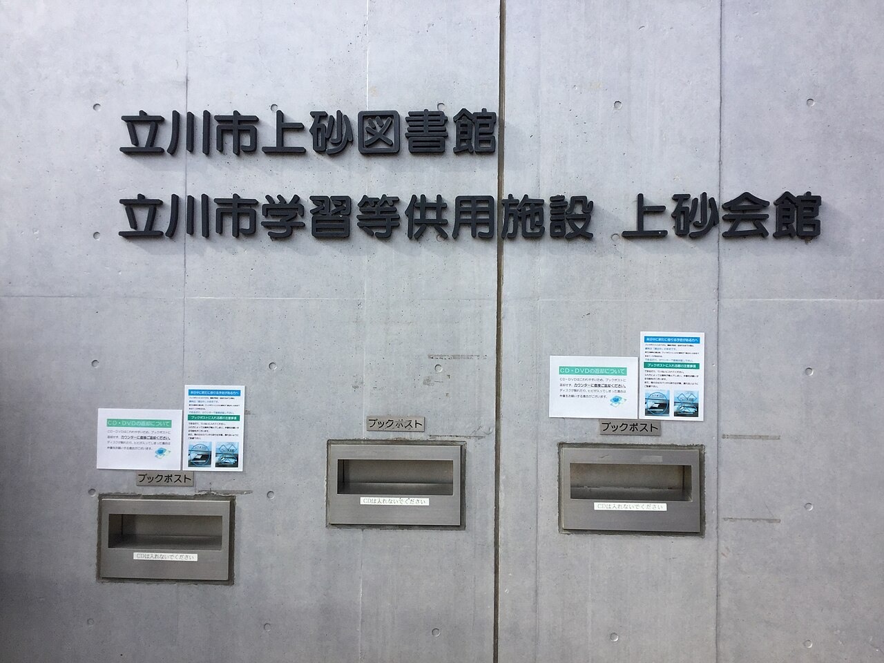 立川市上砂図書館の入口の壁。館名の下に、ブックポストの口が三つ並ぶ。