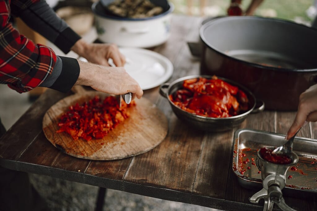 Chopping fresh peppers in a rustic kitchen during a vibrant cooking session in the countryside | オンザショア立川店 立川駅徒歩1分年中無休の溶岩ホットヨガスタジオ 木製のまな板の上で赤いパプリカを刻む手元と調理台に並べられたほかの食材 立川駅徒歩1分年中無休の溶岩ホットヨガスタジオ