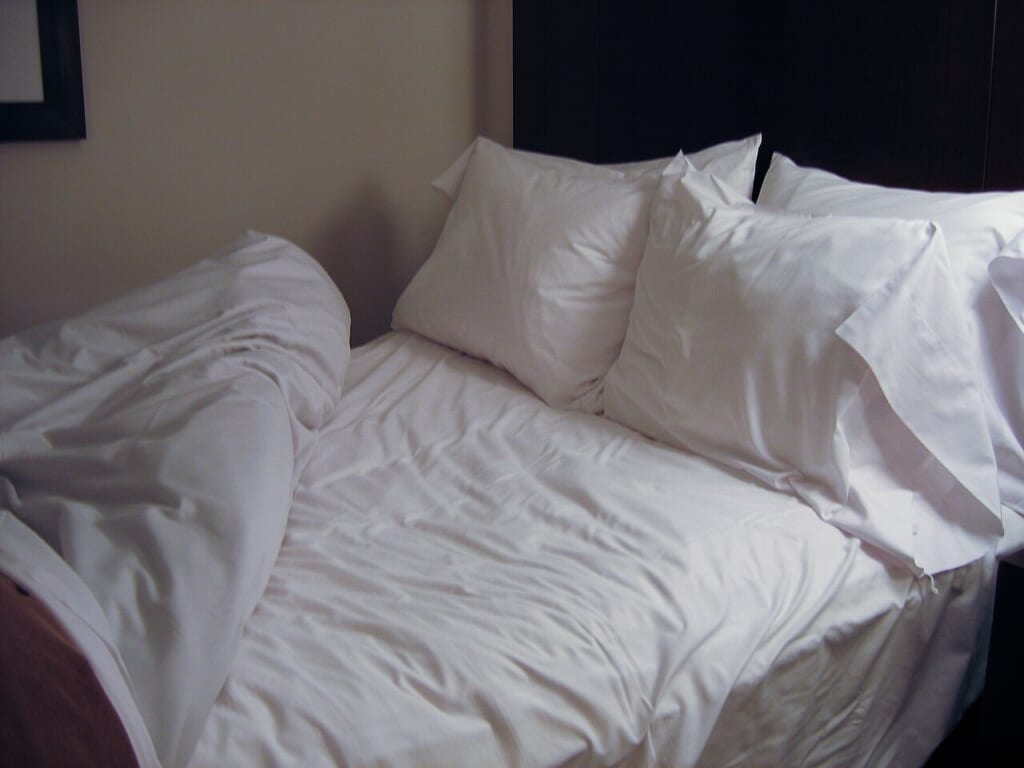 Bed in Seattle hotel | オンザショア立川店 立川駅徒歩1分年中無休の溶岩ホットヨガスタジオ 白いベッドリネンを敷いたベッドに四つのふっくらした枕としわの寄ったシーツがある 立川駅徒歩1分年中無休の溶岩ホットヨガスタジオ
