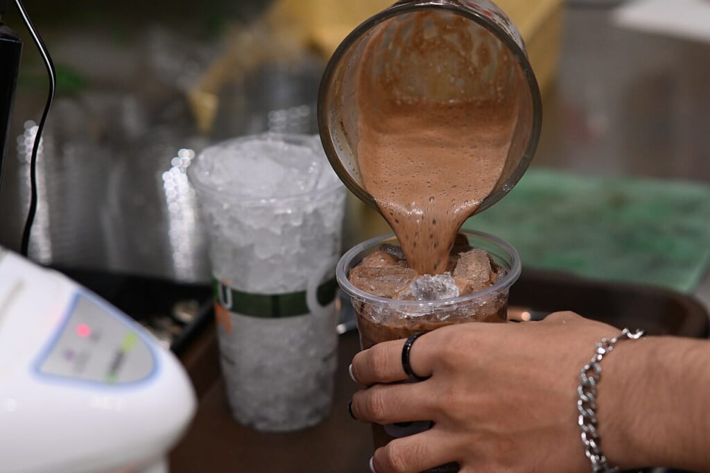 容器からカップへ注がれるチョコレート色の飲み物とカップを持つ手 立川駅徒歩1分年中無休の溶岩ホットヨガスタジオ
