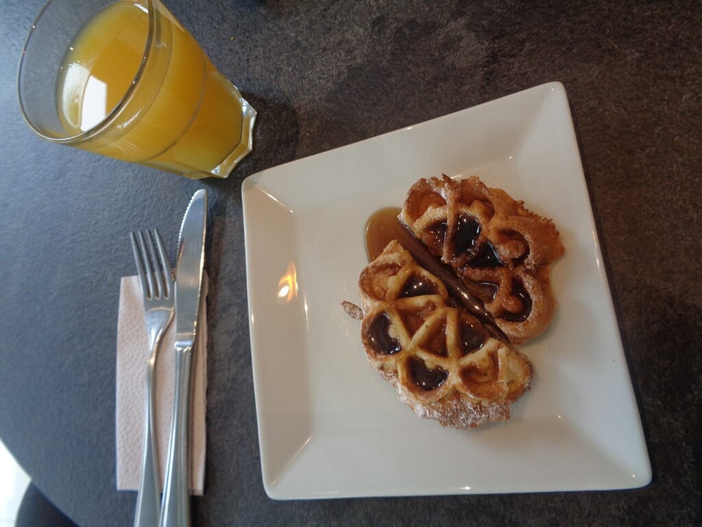 a glass of orange juice a waffle on a nice plate with silverware | オンザショア立川店 立川駅徒歩1分年中無休の溶岩ホットヨガスタジオ グラスに入ったオレンジジュースとカトラリーを添えた皿の上のワッフル 立川駅徒歩1分年中無休の溶岩ホットヨガスタジオ