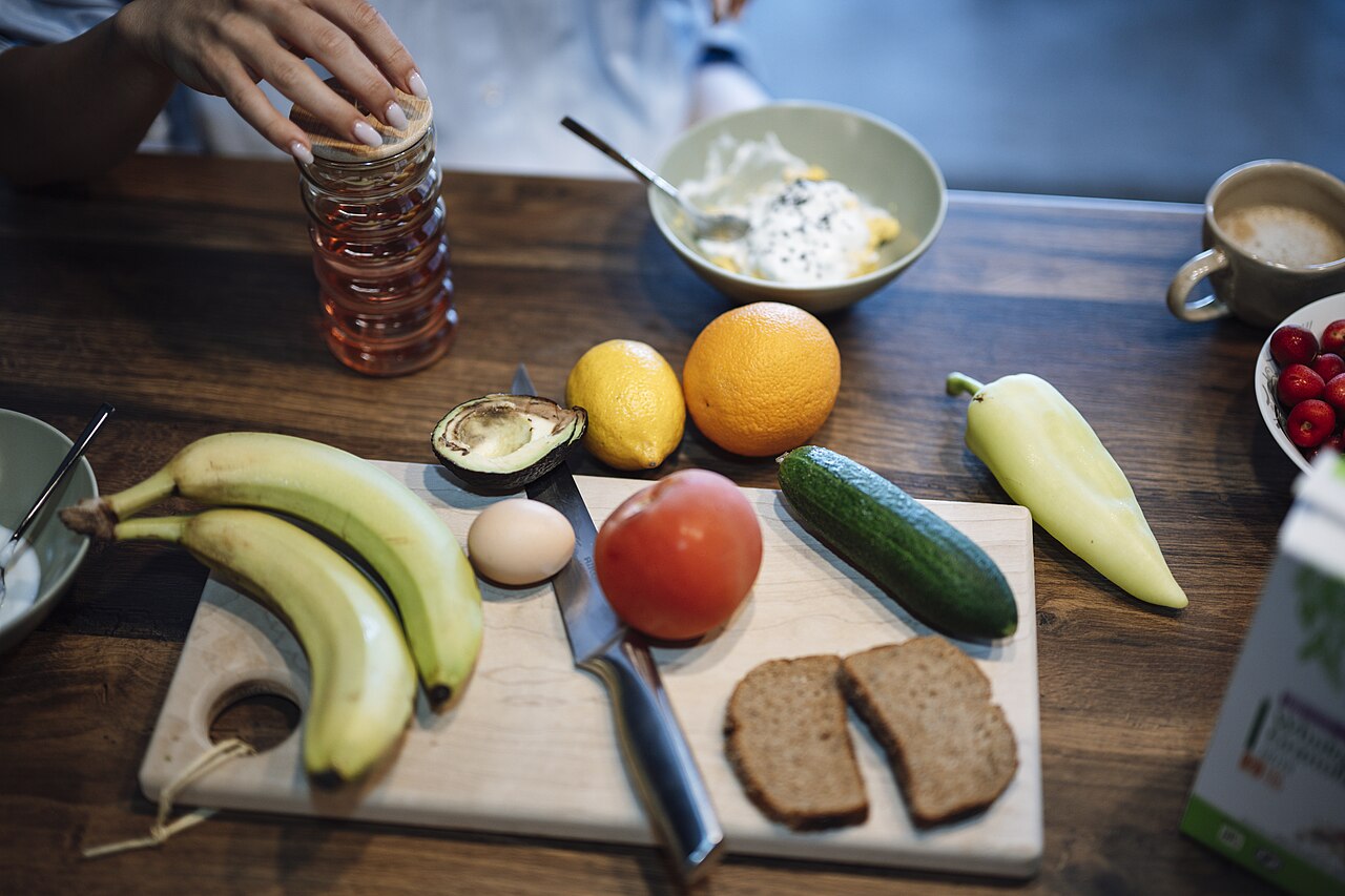 Fruit, vegetables, bread, and a yogurt bowl are arranged on a wooden breakfast table.