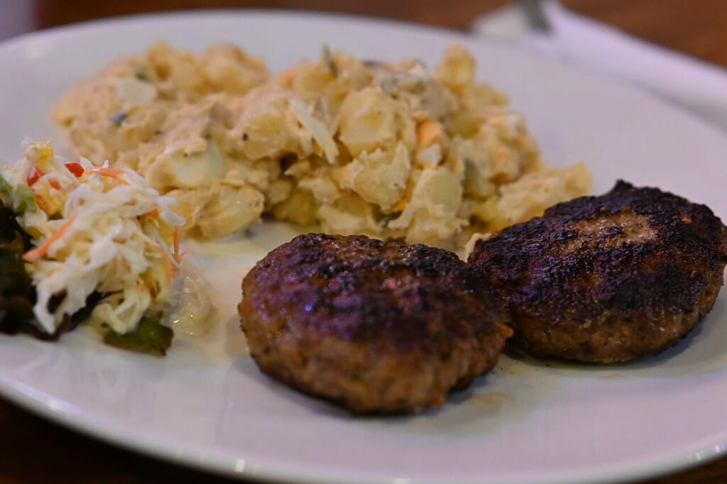 DFC 0879 Two seasoned beef patties served with creamy potato salad and a side of coleslaw on a white dinner plate | オンザショア立川店 立川駅徒歩1分年中無休の溶岩ホットヨガスタジオ 白い皿に盛られた2枚の牛肉のパティとポテトサラダコールスロー 立川駅徒歩1分年中無休の溶岩ホットヨガスタジオ