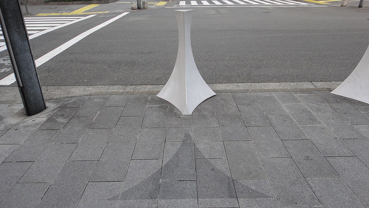 A slender white bollard on a Faret Tachikawa pavement, symmetrical from top to bottom and side to side