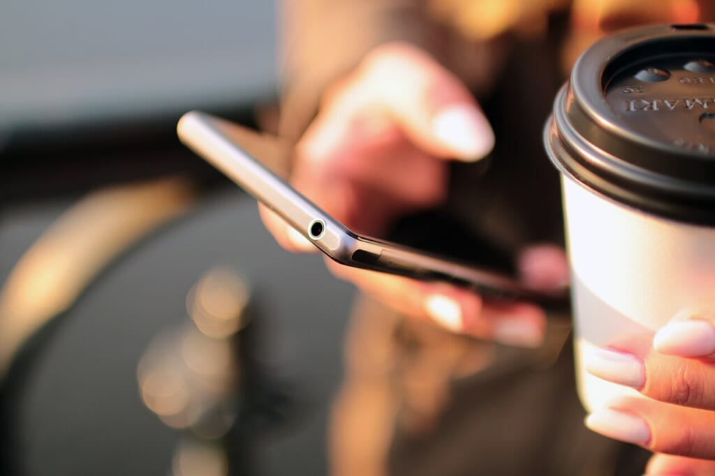 スマートフォンを手にした人の手元とコーヒーを一緒に写した写真 立川駅徒歩1分年中無休の溶岩ホットヨガスタジオ