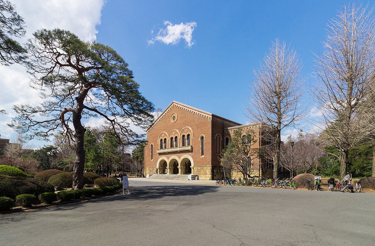 Kanematsu Auditorium at Hitotsubashi University, a Romanesque-style building by Chuta Ito, seen beyond pine trees.