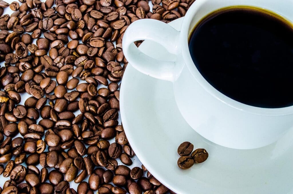 Coffee cup and coffee bean | オンザショア立川店 立川駅徒歩1分年中無休の溶岩ホットヨガスタジオ コーヒーカップとそのそばに置かれた茶色いコーヒー豆を写した写真 立川駅徒歩1分年中無休の溶岩ホットヨガスタジオ