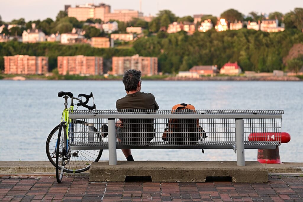 Man on a bench by the river with a bicycle Quebec City | オンザショア立川店 立川駅徒歩1分年中無休の溶岩ホットヨガスタジオ 川沿いのベンチに一人で座る人物と傍らに立てかけられた自転車のある風景 立川駅徒歩1分年中無休の溶岩ホットヨガスタジオ