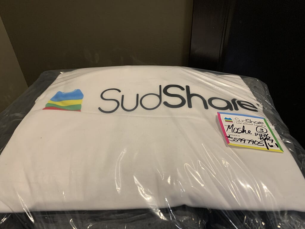 Bag of clean laundry from a SudShare order 01 | オンザショア立川店 立川駅徒歩1分年中無休の溶岩ホットヨガスタジオ 玄関の外に置かれた透明な袋入りの洗濯物とその上に添えられた手書きのメモ 立川駅徒歩1分年中無休の溶岩ホットヨガスタジオ