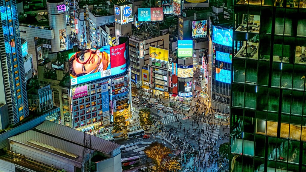 建物の上から見下ろした交差点と横断歩道を行き交う人々を遠くに捉えた街の風景 立川駅徒歩1分年中無休の溶岩ホットヨガスタジオ