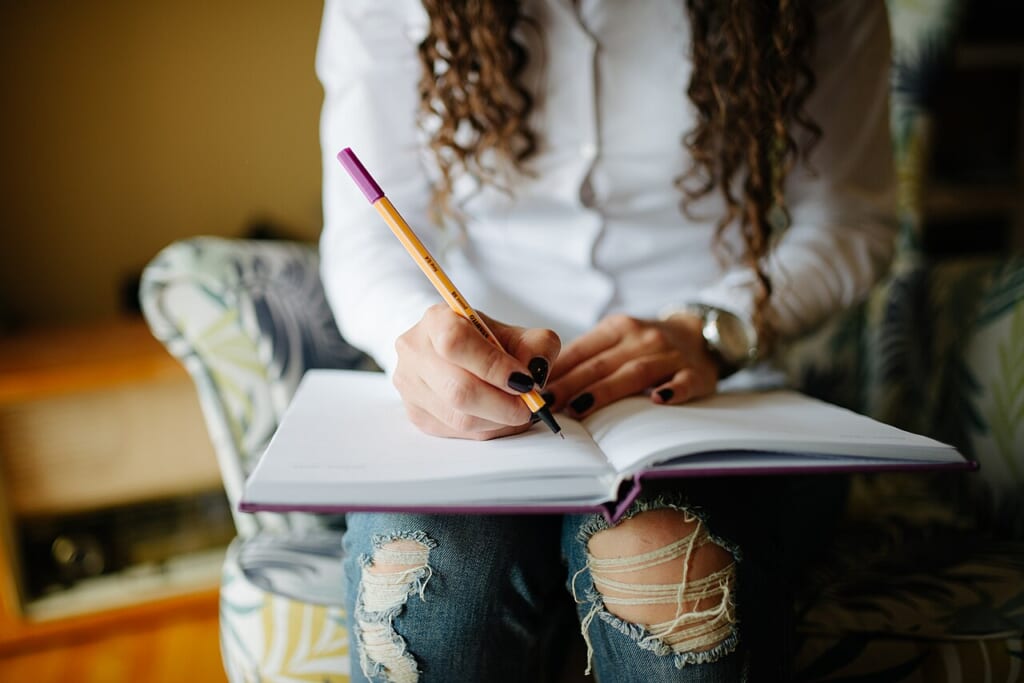 Hands of a woman writing notes in her planner closeup | オンザショア立川店 立川駅徒歩1分年中無休の溶岩ホットヨガスタジオ 開いた手帳にペンで書き込んでいる手元を近くからとらえた横長の写真 立川駅徒歩1分年中無休の溶岩ホットヨガスタジオ