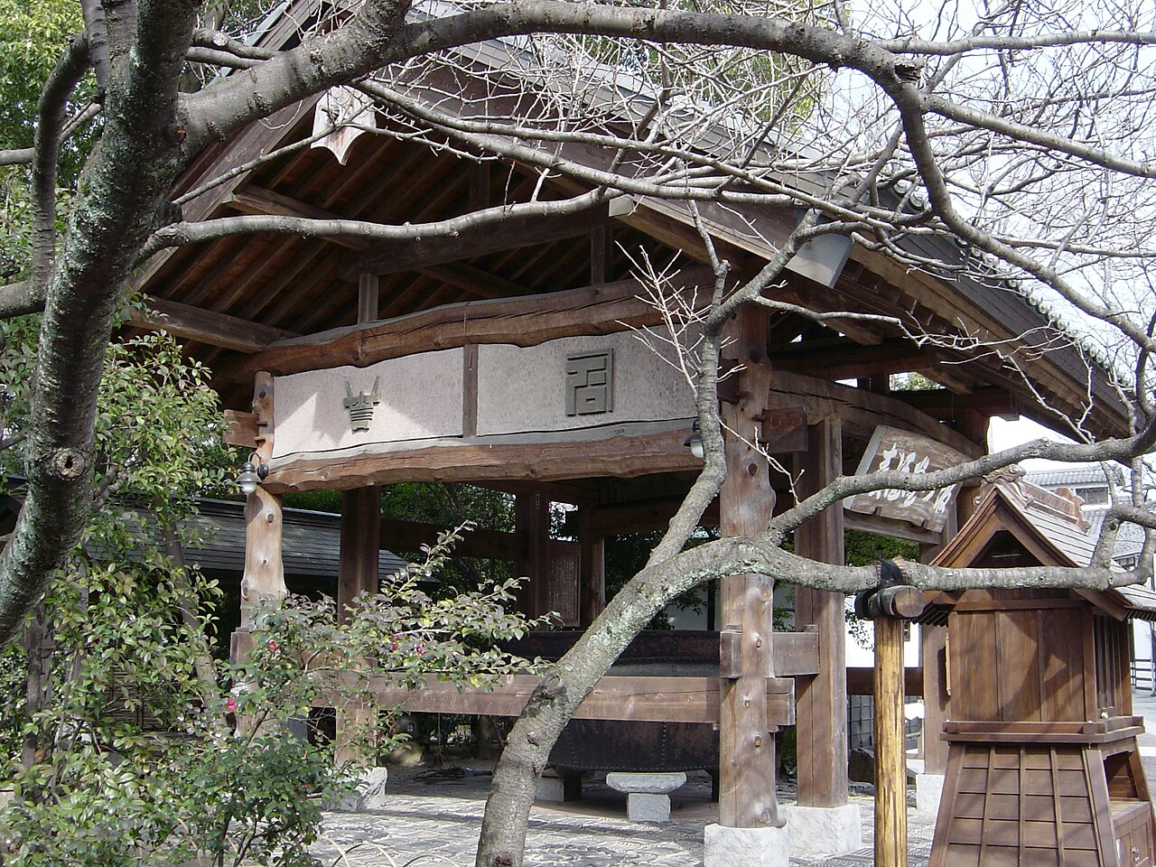 A timber-framed roofed structure in the grounds of Ishikawa Brewery, seen through bare winter branches.