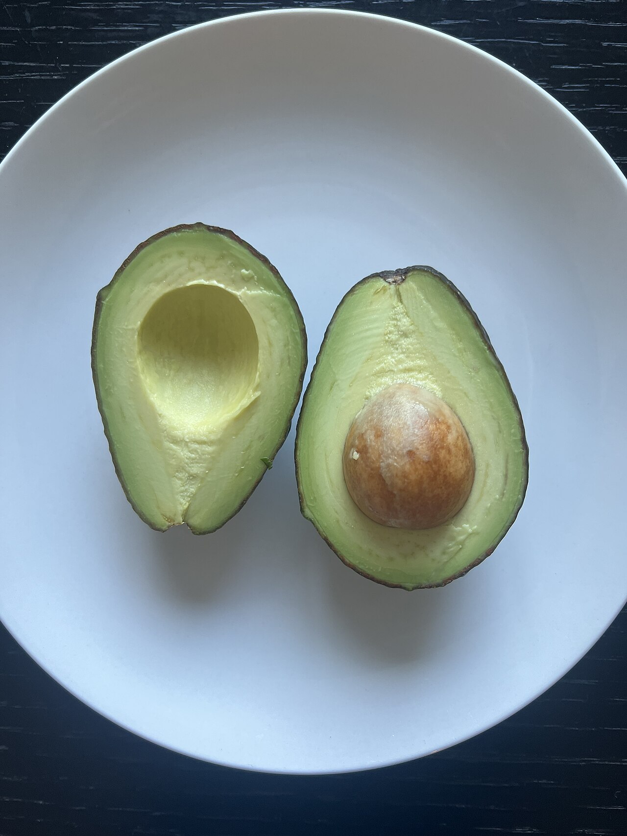 白い皿に並べられた二つ割りのアボカド。片方には種が残り、もう片方は種がない。