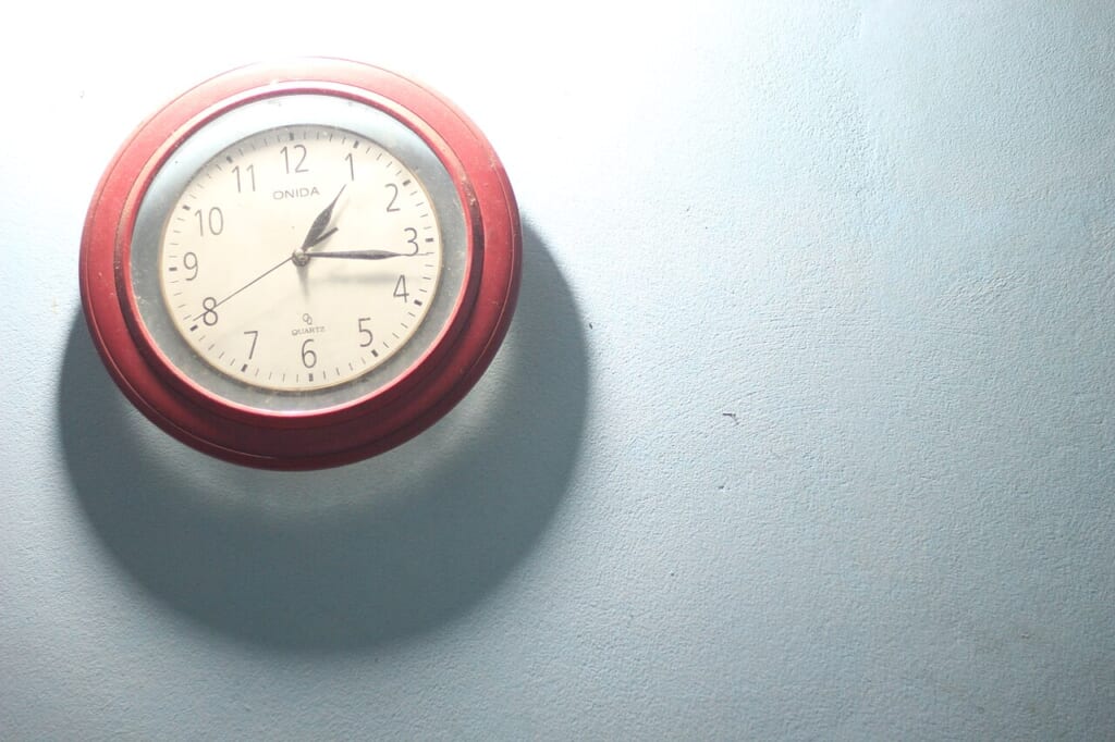 Analog Clock | オンザショア立川店 立川駅徒歩1分年中無休の溶岩ホットヨガスタジオ 時刻を示す針と文字盤を備えた壁に掛けて使うアナログ時計の写真 立川駅徒歩1分年中無休の溶岩ホットヨガスタジオ