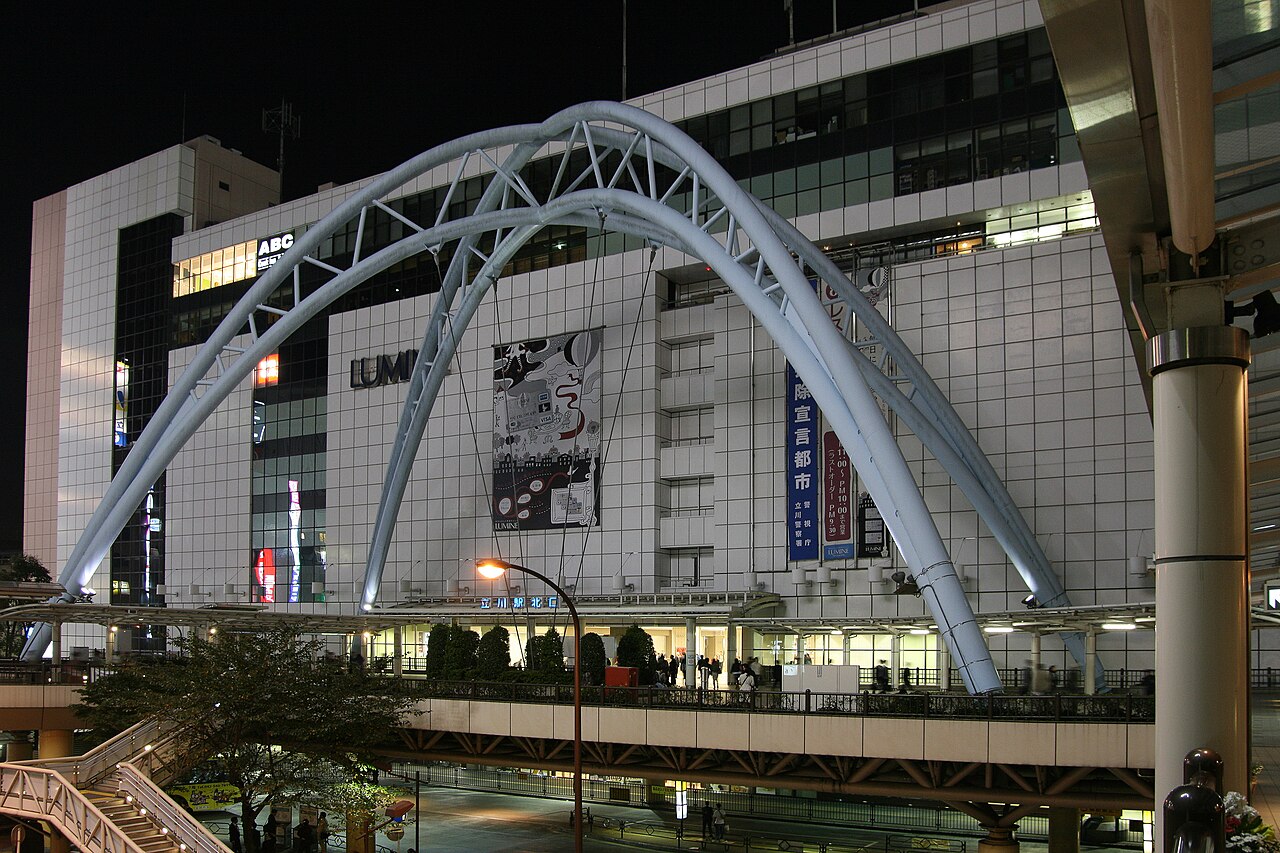 日暮れの立川駅北口。デッキのアーチの奥に、窓の明かりがともる駅ビルが見える。