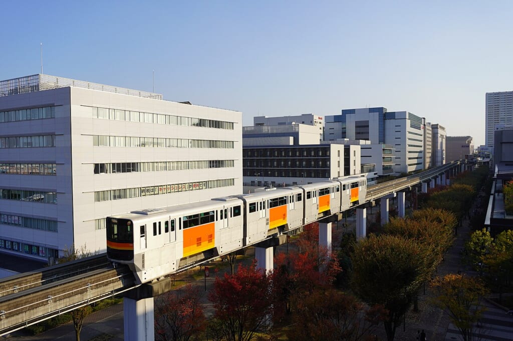 GREEN SPRINGSから見た多摩モノレール紅葉した木々の上の軌道を車両が走っていく 立川駅徒歩1分年中無休の溶岩ホットヨガスタジオ