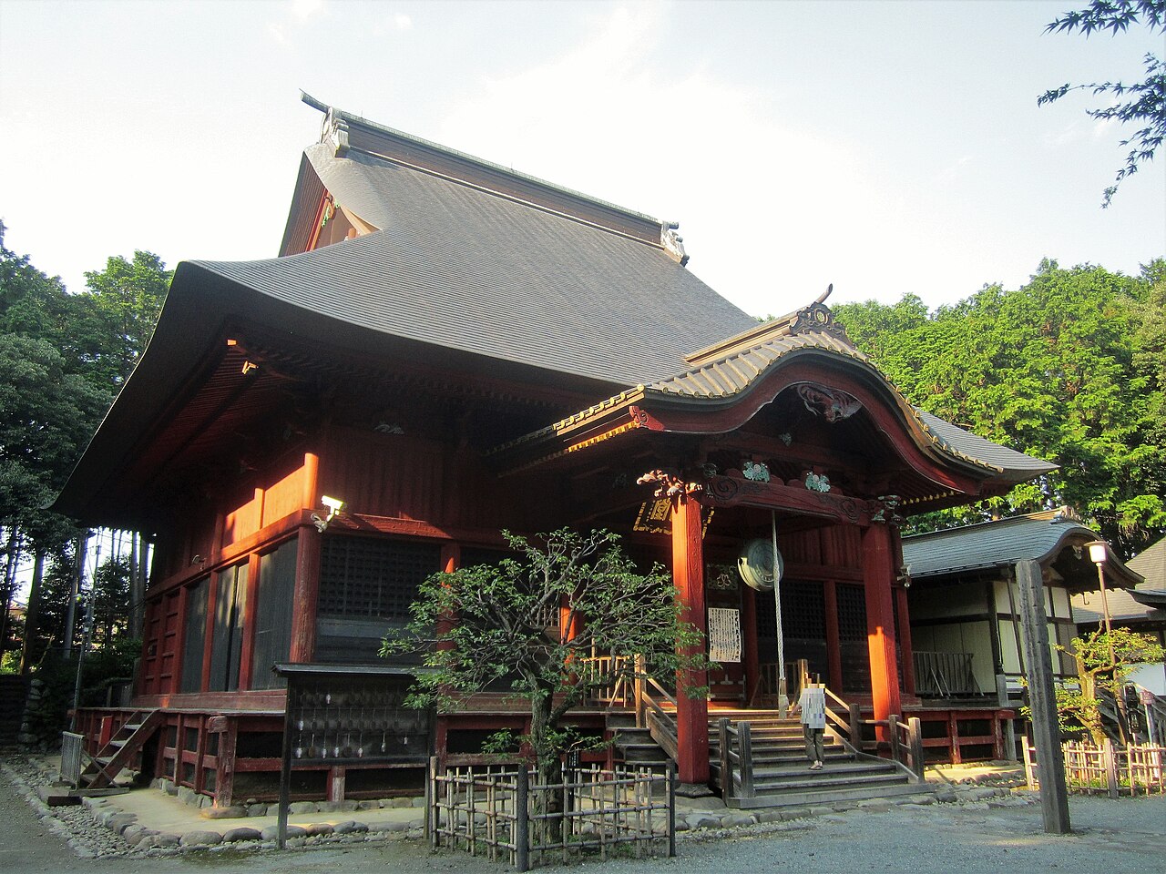The Dainichi-do hall in Haijima-cho, Akishima, with vermilion pillars and a broad roof before the trees.