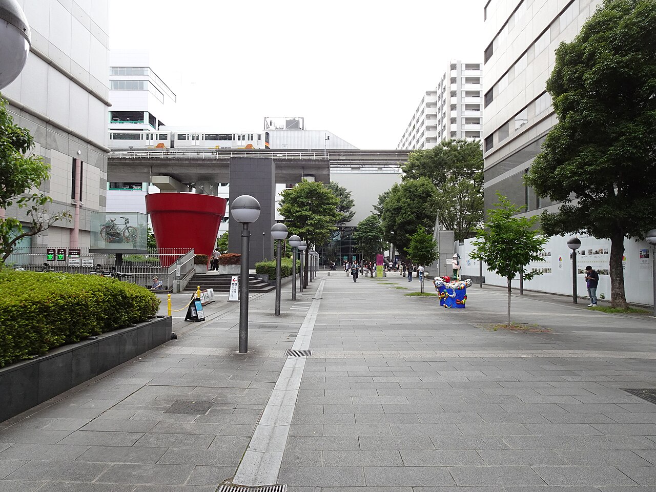 A Faret Tachikawa walkway where a large red flowerpot stands between street trees and lamps