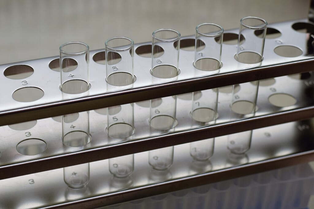 Test tubes in rack | オンザショア立川店 立川駅徒歩1分年中無休の溶岩ホットヨガスタジオ 研究室で使われる試験管を金属製のラックに立てて並べた実験器具の写真 立川駅徒歩1分年中無休の溶岩ホットヨガスタジオ