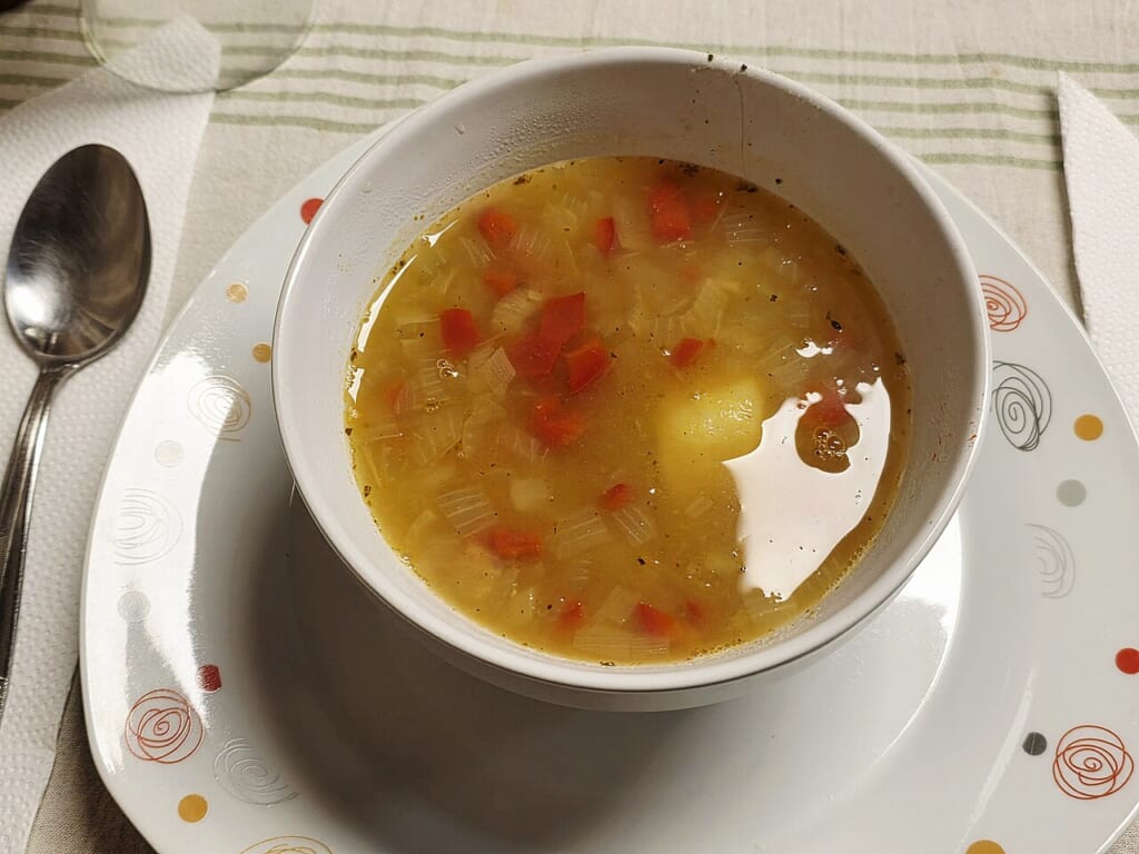 Argentine Homemade Vegetable Soup | オンザショア立川店 立川駅徒歩1分年中無休の溶岩ホットヨガスタジオ 白い器に盛られた赤いピーマンや玉ねぎじゃがいもが入った淡い黄金色の野菜スープ 立川駅徒歩1分年中無休の溶岩ホットヨガスタジオ
