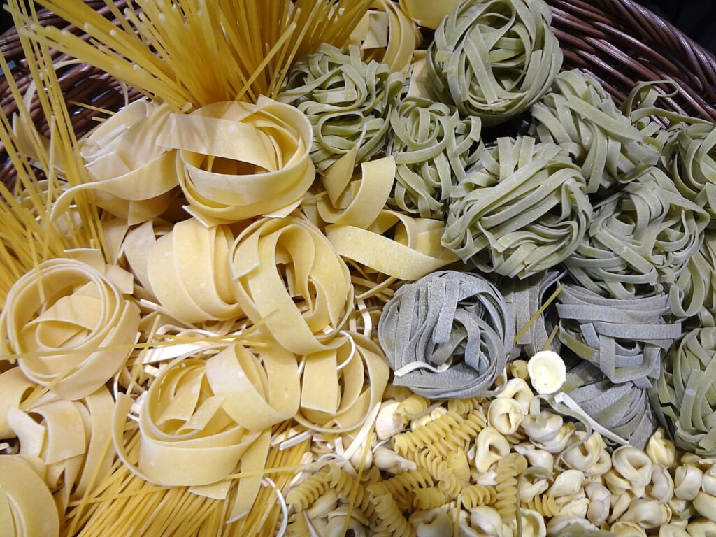 かごに盛られた黄色や緑の平たいパスタを丸めたものスパゲッティねじれたパスタなど数種類のパスタ 立川駅徒歩1分年中無休の溶岩ホットヨガスタジオ