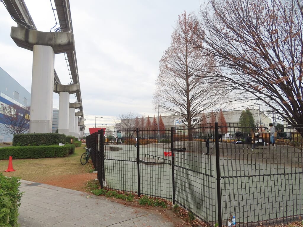 たちかわ中央公園スケートパーク柵の向こうに滑走面があり左手にモノレールの高架が見える 立川駅徒歩1分年中無休の溶岩ホットヨガスタジオ