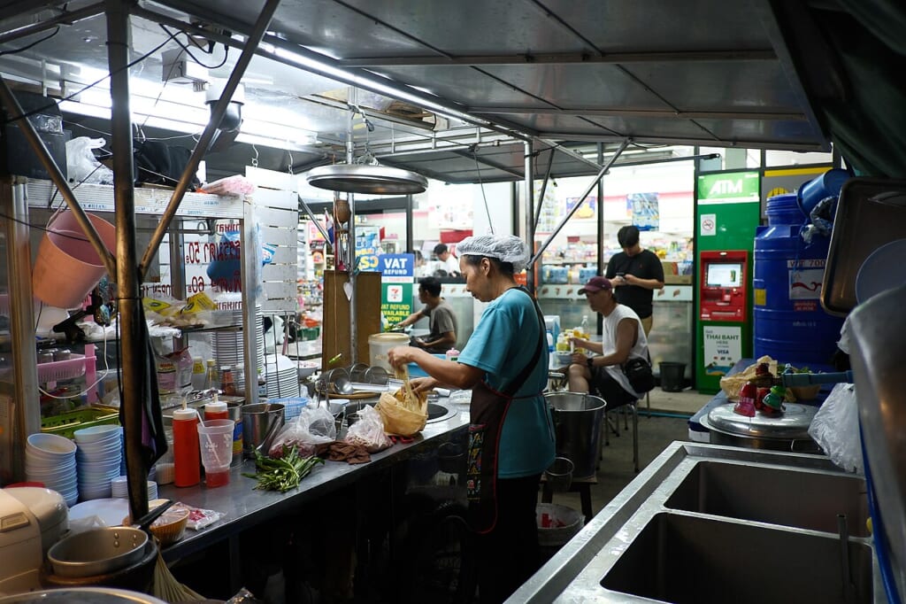 明るく照らされた屋台の厨房でエプロンを着けた人が料理の準備をしている様子 立川駅徒歩1分年中無休の溶岩ホットヨガスタジオ