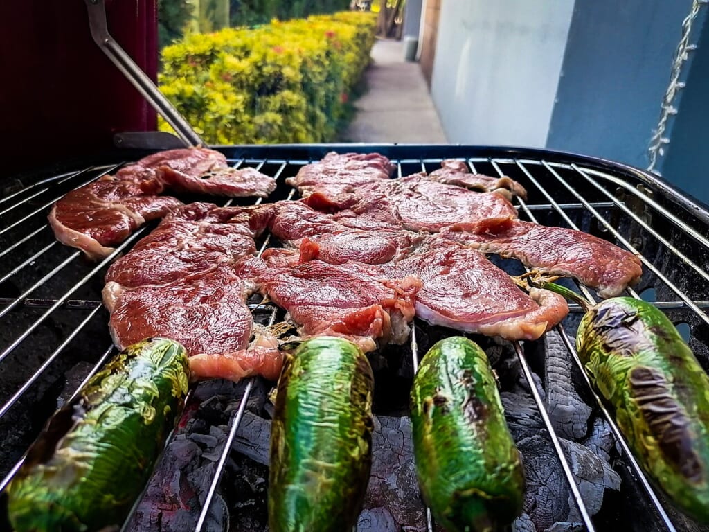 Asando carne y chile jalapeño en parrilla al carbón | オンザショア立川店 立川駅徒歩1分年中無休の溶岩ホットヨガスタジオ 炭火の焼き網の上で牛肉とハラペーニョを一緒に焼いている様子 立川駅徒歩1分年中無休の溶岩ホットヨガスタジオ