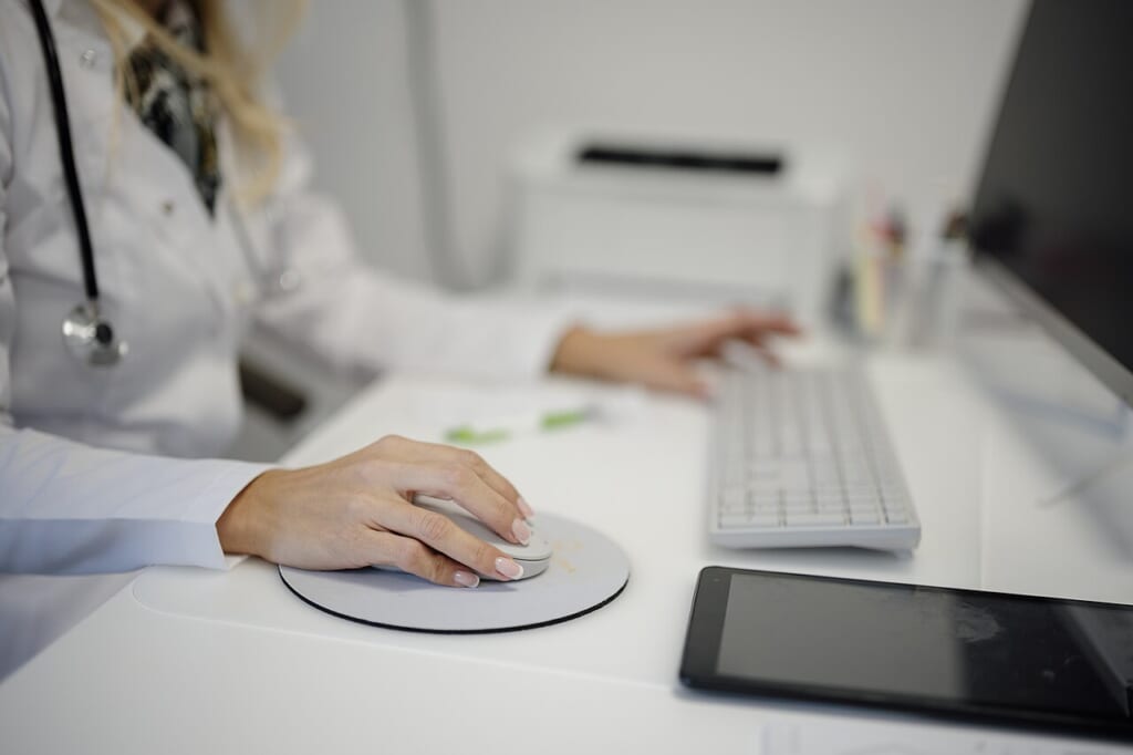 Doctor working at a desk using a computer mouse and keyboard in a medical office setting | オンザショア立川店 立川駅徒歩1分年中無休の溶岩ホットヨガスタジオ 机の上でマウスとキーボードを操作している人の手元を写した写真 立川駅徒歩1分年中無休の溶岩ホットヨガスタジオ