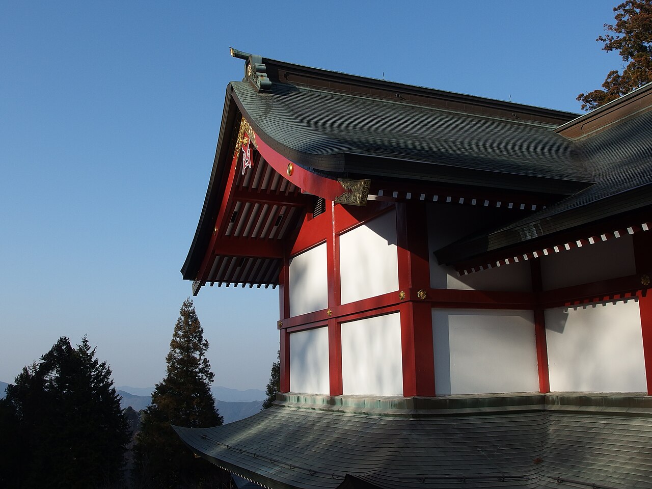 Part of a shrine building at Musashi Mitake Shrine, vermilion pillars and white walls against a blue sky.