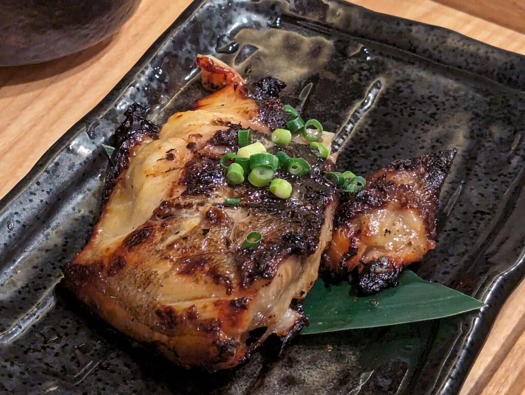 黒い角皿に盛られた焼き魚の切り身上に刻んだ青ねぎがのせてある 立川駅徒歩1分年中無休の溶岩ホットヨガスタジオ