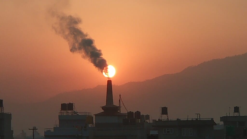 れんが工場の煙突から煙が立ち上り背後の太陽の一部が煙に覆われている 立川駅徒歩1分年中無休の溶岩ホットヨガスタジオ