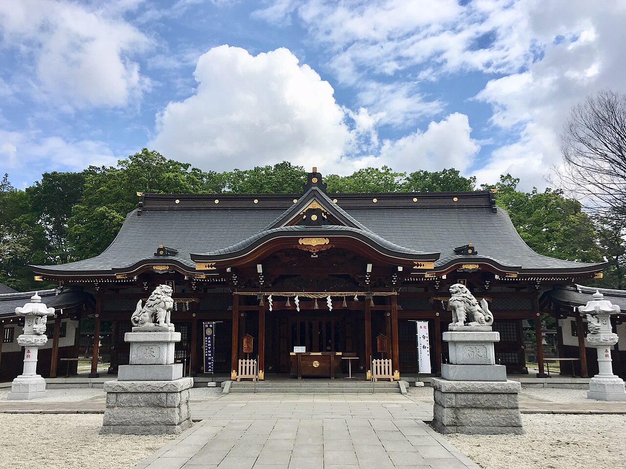 立川の諏訪神社の社殿。青空と白い雲の下、狛犬と灯籠が参道の両脇に並ぶ。