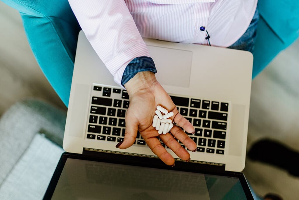Closeup of the pills in a woman s hand and laptop on her lap | オンザショア立川店 立川駅徒歩1分年中無休の溶岩ホットヨガスタジオ 手のひらに載せた錠剤と膝の上に置かれたノートパソコンの接写写真 立川駅徒歩1分年中無休の溶岩ホットヨガスタジオ