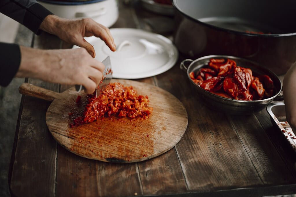 Chopping vegetables and preparing spices for a traditional meal | オンザショア立川店 立川駅徒歩1分年中無休の溶岩ホットヨガスタジオ 木のまな板の上で赤い野菜を刻む手と周りに置かれた食材入りの器 立川駅徒歩1分年中無休の溶岩ホットヨガスタジオ