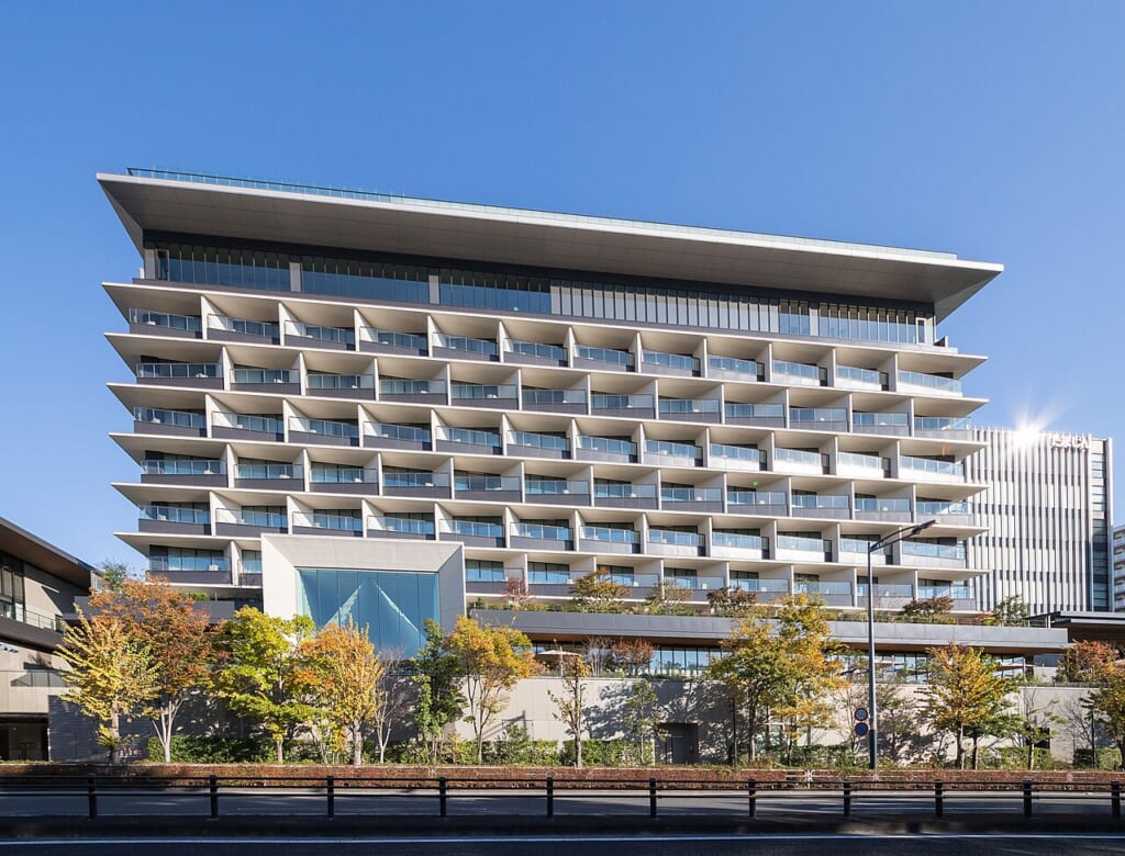SORANO HOTEL | オンザショア立川店 立川駅徒歩1分年中無休の溶岩ホットヨガスタジオ GREEN SPRINGSのSORANO HOTEL白い横縞のバルコニーが重なる建物が青空の下に立つ 立川駅徒歩1分年中無休の溶岩ホットヨガスタジオ