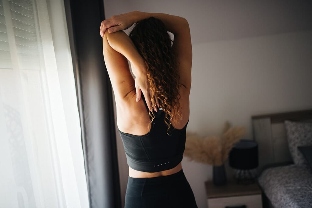 Back view of a woman performing a stretching exercise for the spine | オンザショア立川店 立川駅徒歩1分年中無休の溶岩ホットヨガスタジオ 背中を伸ばすストレッチ運動を行っている女性を背後から捉えた写真 立川駅徒歩1分年中無休の溶岩ホットヨガスタジオ