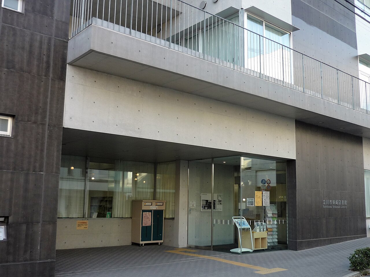立川市柴崎図書館の入口。打ち放しのコンクリートの建物の1階に、ガラスの扉が開く。