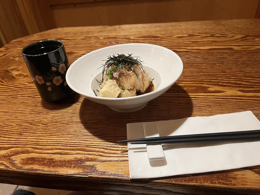 器に盛られた揚げ出し豆腐とそのそばに置かれたお茶と箸が写っている 立川駅徒歩1分年中無休の溶岩ホットヨガスタジオ