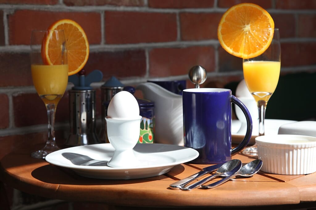 Hard boiled egg on breakfast table | オンザショア立川店 立川駅徒歩1分年中無休の溶岩ホットヨガスタジオ 白いエッグカップに入ったゆで卵とコーヒーカップやオレンジジュースが並ぶ朝食の食卓 立川駅徒歩1分年中無休の溶岩ホットヨガスタジオ