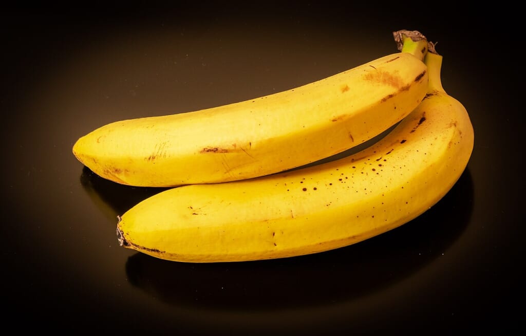 Bananas on black background 02 | オンザショア立川店 立川駅徒歩1分年中無休の溶岩ホットヨガスタジオ 黒い背景の前に置かれたバナナを果実の形や表面が見えるように写した写真 立川駅徒歩1分年中無休の溶岩ホットヨガスタジオ